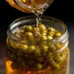 Easy Homemade Caperberries Recipe in 30 Minutes 10 homemade caperberries in a glass jar with hot brine being poured in.